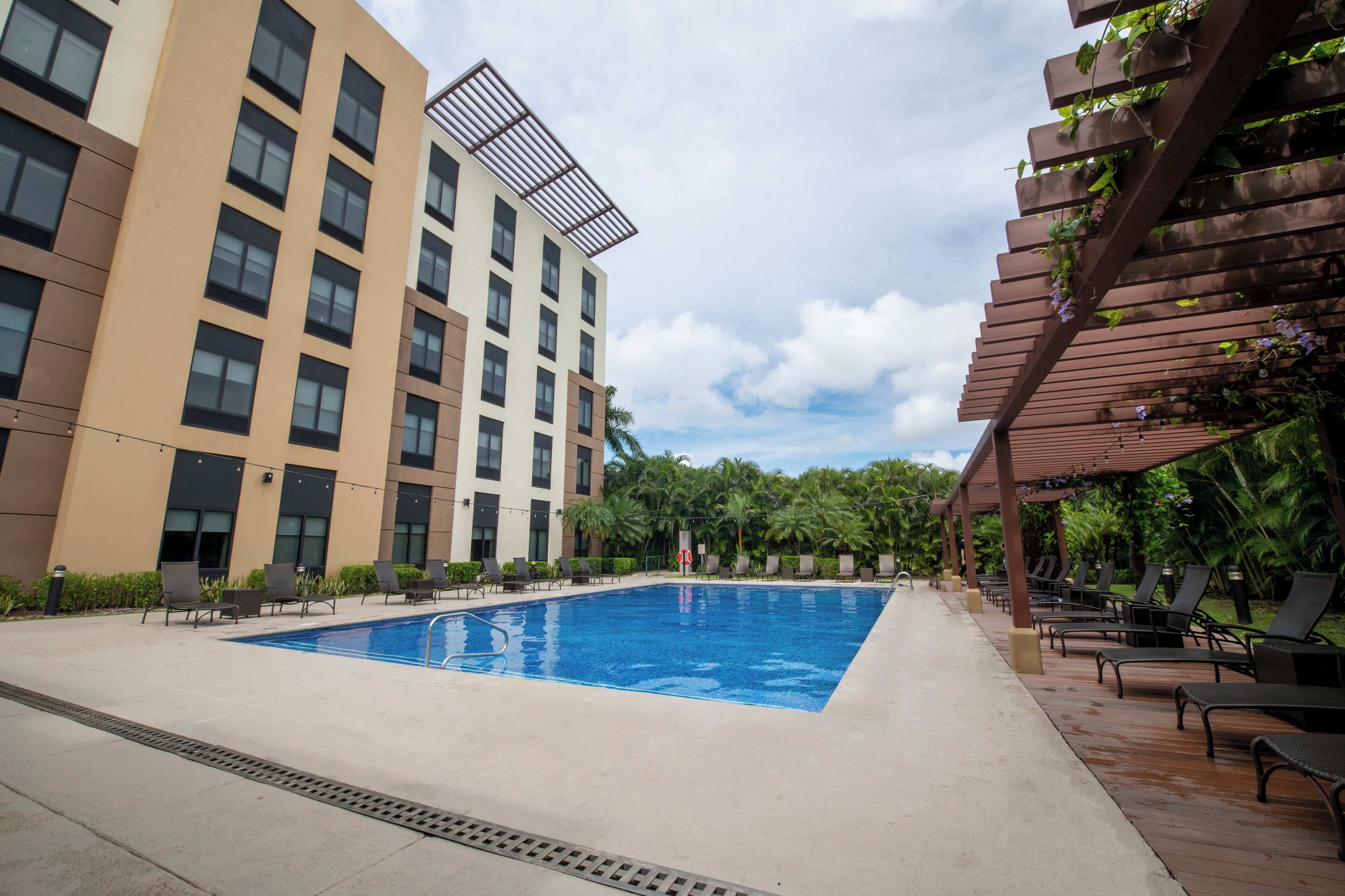 Piscina com espreguiçadeiras e um edifício com vários andares e varandas.