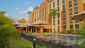 A hotel with a swimming pool, sun loungers, and palm trees.
