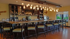 A bar area with wooden flooring, bar stools, and a long counter with a television.