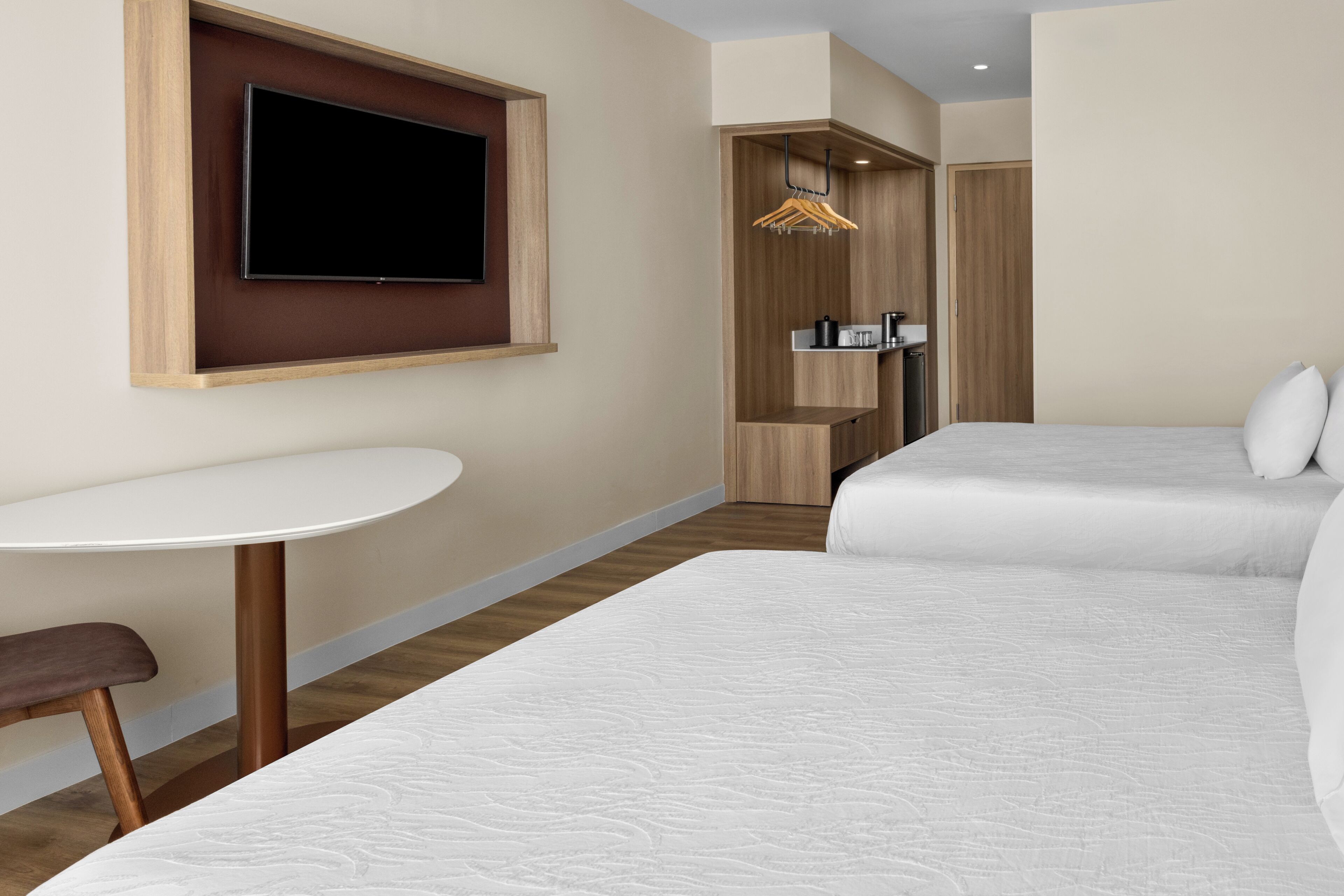 Ein Hotelzimmer mit zwei Betten, einem kleinen Tisch, einem an der Wand montierten Fernseher und einem Kleiderschrank mit Spiegel.