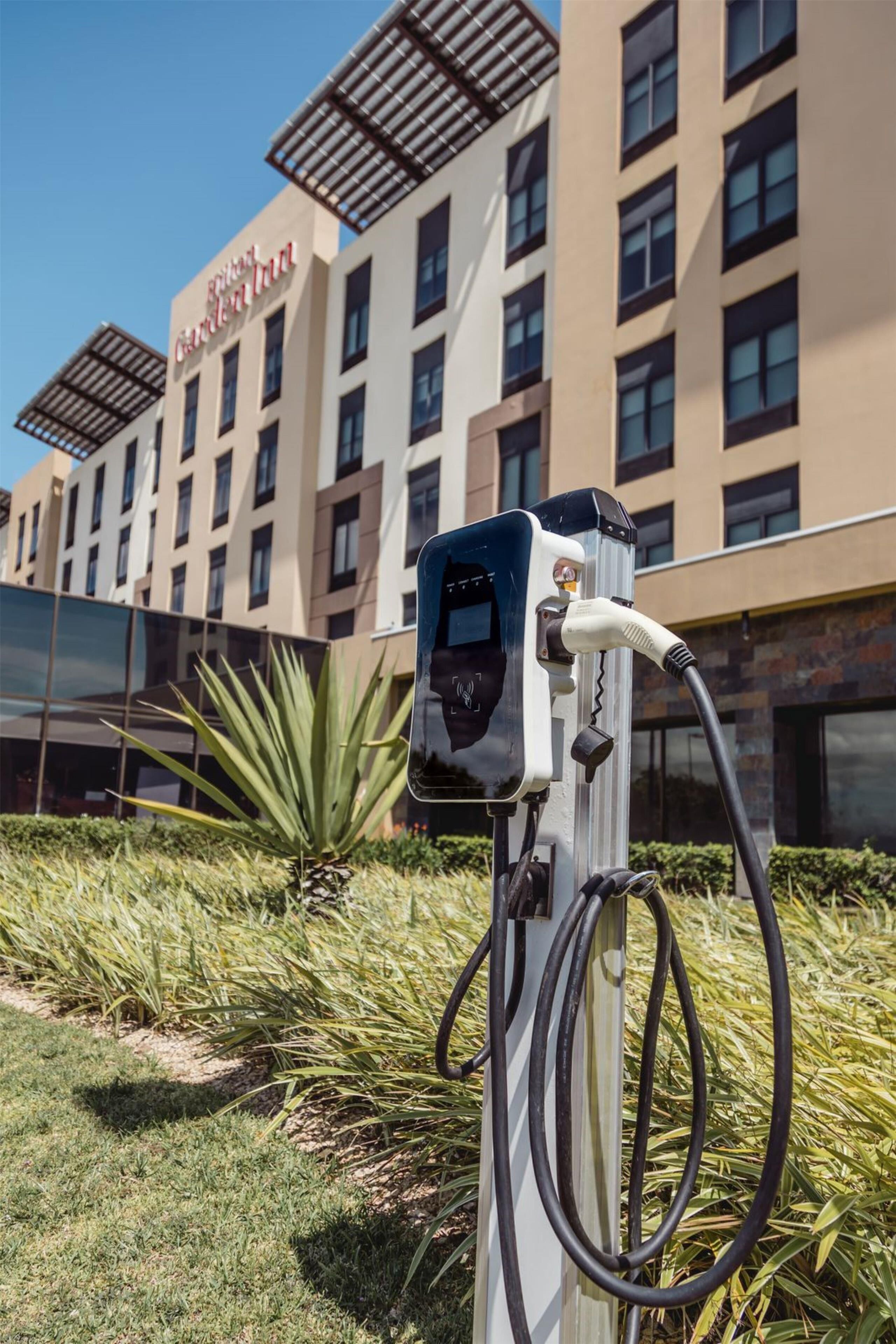 A charging station in front of a hotel with a modern design, a clear sky, and a well-maintained lawn.