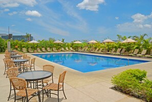 A pool area with lounge chairs and tables, surrounded by palm trees and umbrellas. - Hilton Garden Inn Guanacaste Airport  (Liberia)