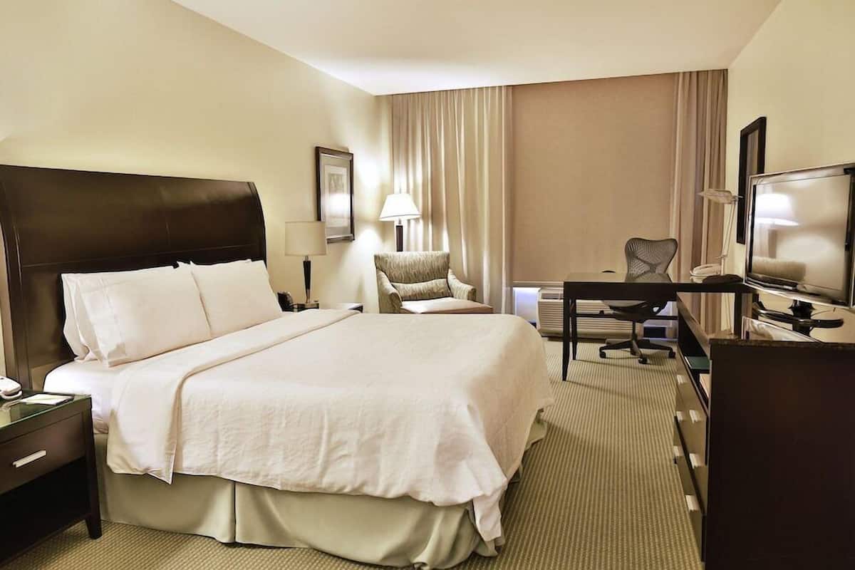 Une chambre d’hôtel avec un grand lit, un bureau avec une chaise, une télévision et une lampe.