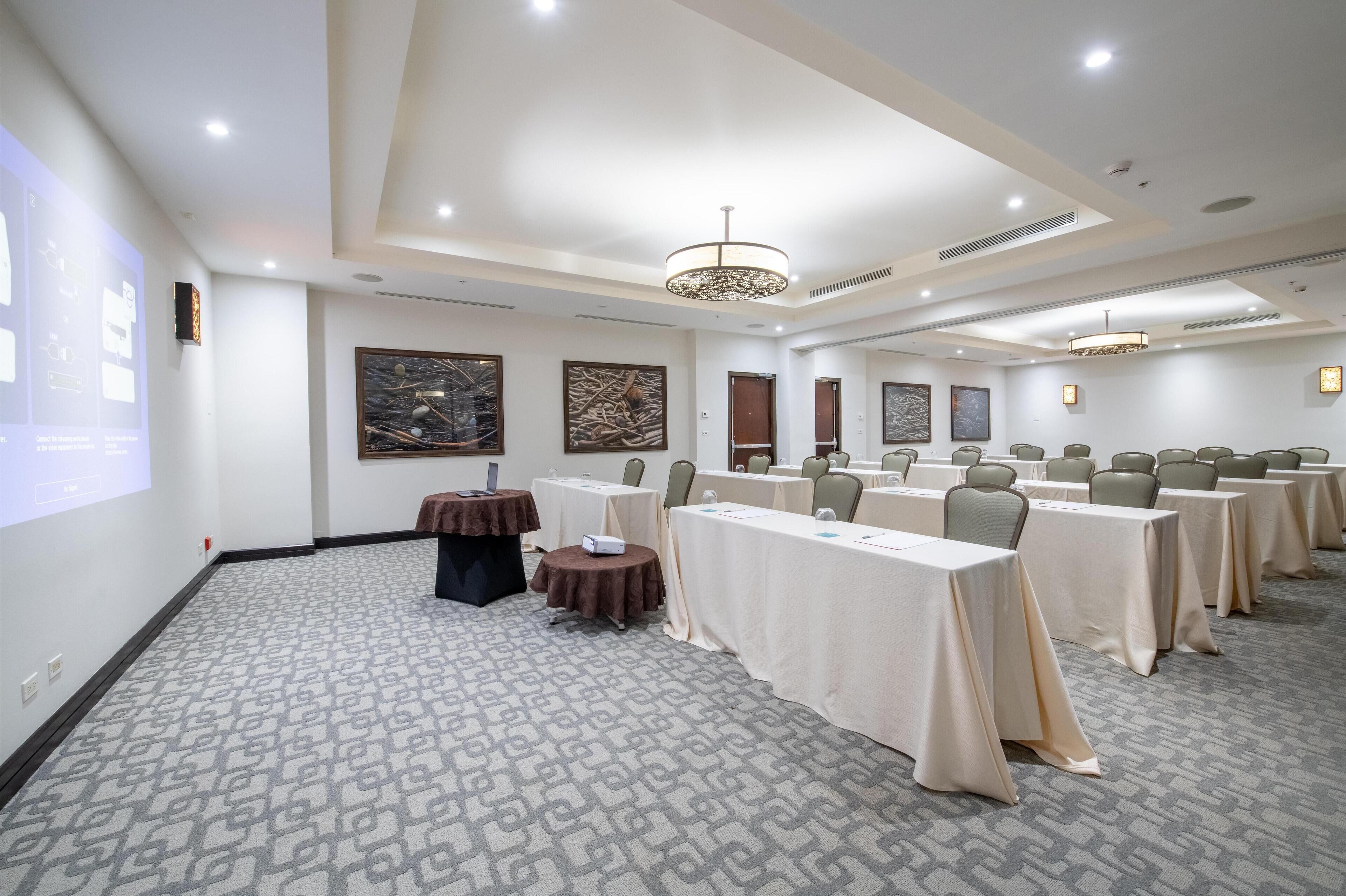 A conference room with tables, chairs, a projector screen, and artwork on the walls.