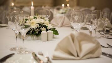 Una mesa dispuesta para un evento formal, con manteles blancos, copas de cristal transparente y un centro de mesa con flores y velas blancas.