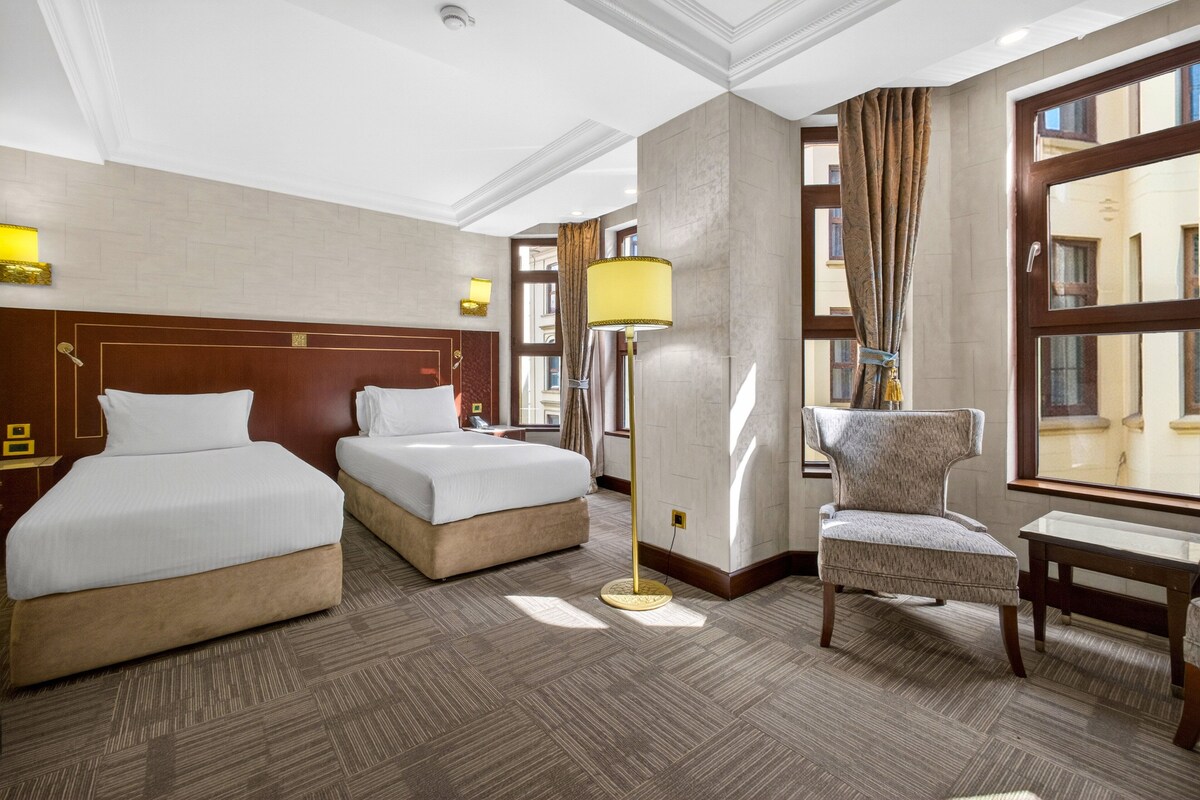 Een hotelkamer met twee bedden, een stoel, een lamp en een groot raam.