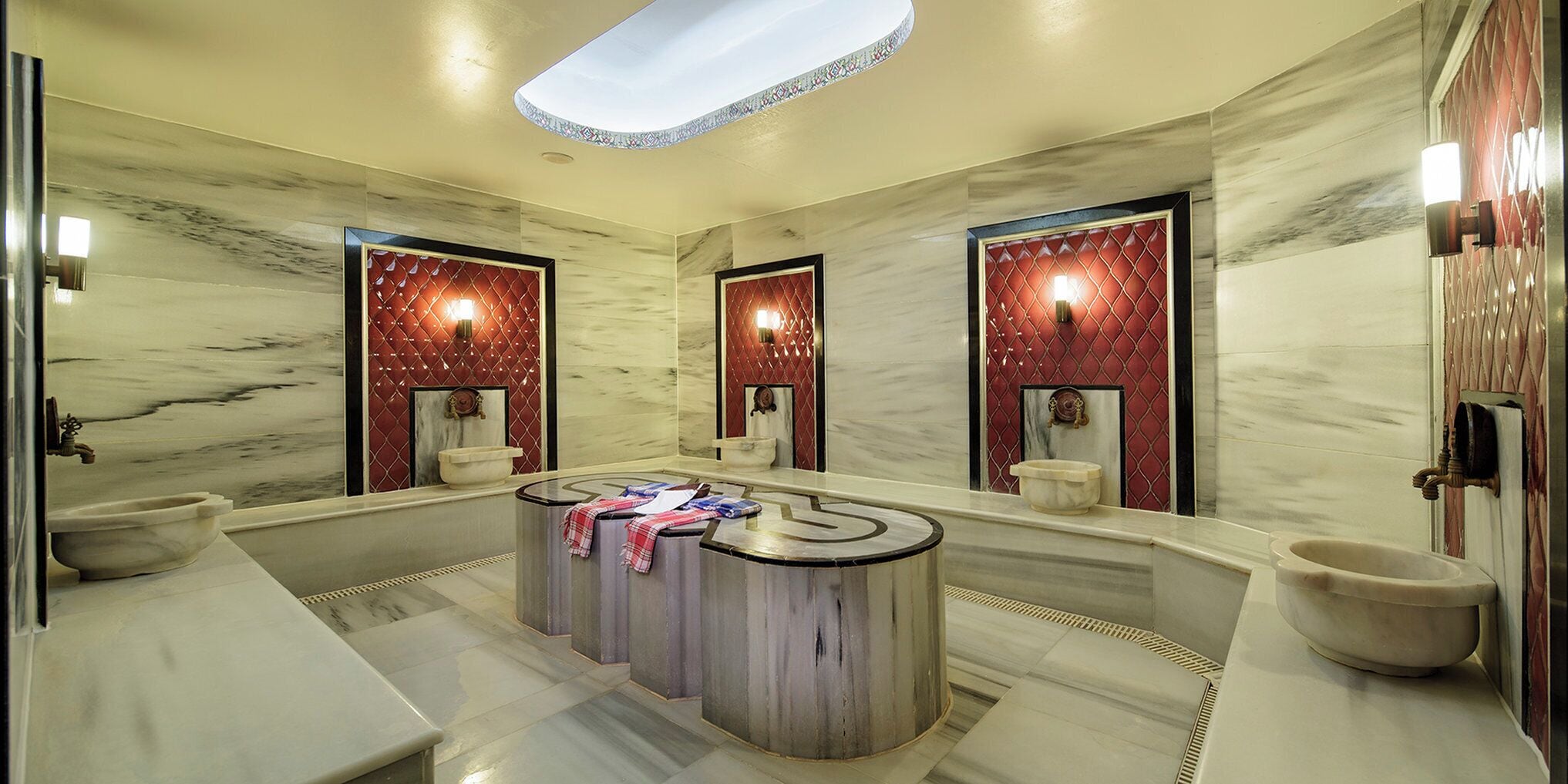 Un baño lujoso con suelo de mármol, un lavabo redondo central y dos lavamanos amplios empotrados.