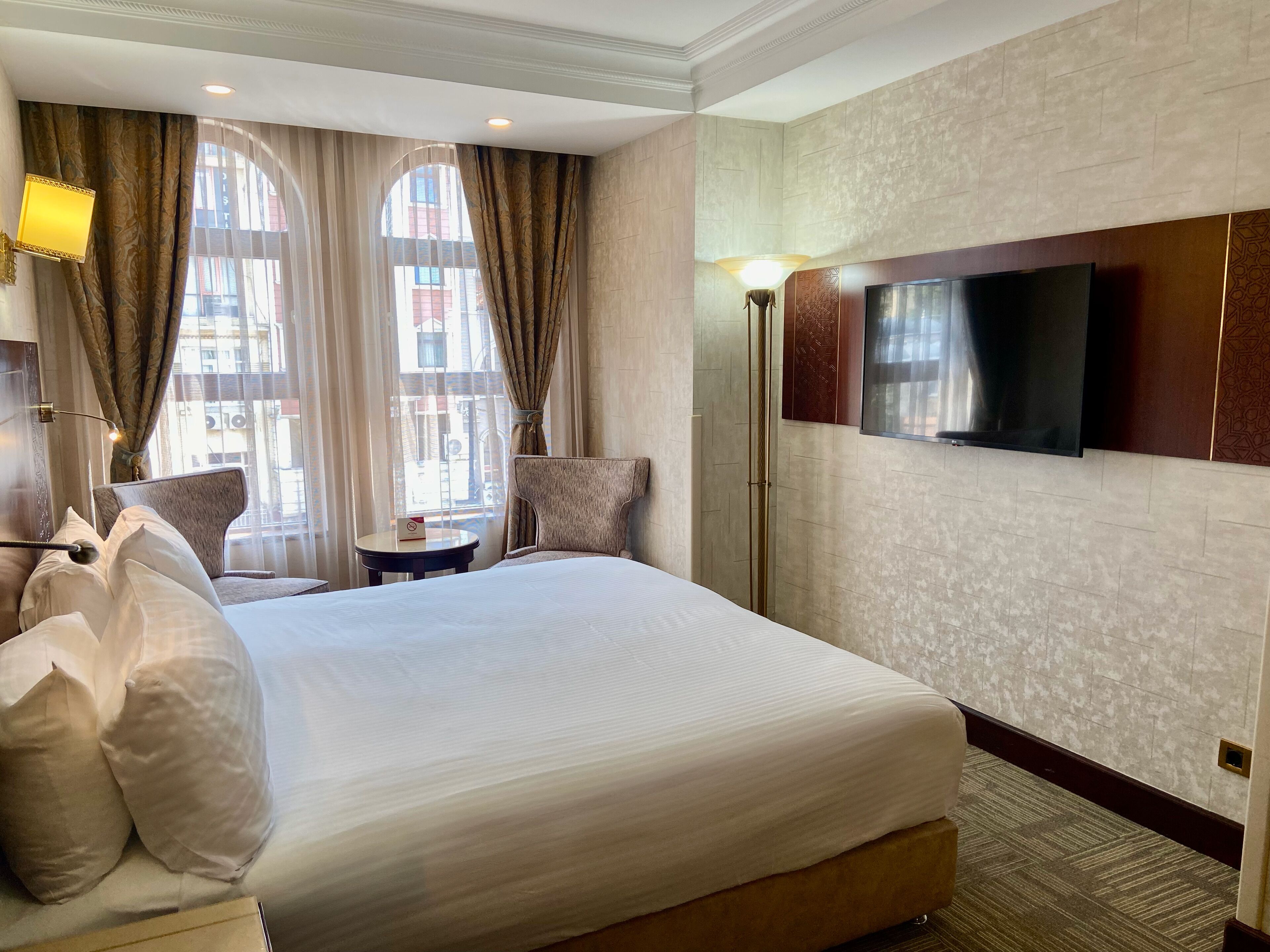 Une chambre d’hôtel avec un grand lit, un téléviseur fixé au mur, une chaise et une petite table.