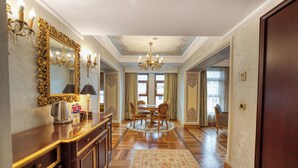 Een ruime kamer met een houten vloer, een ronde eettafel met stoelen, een kroonluchter en een grote spiegel aan de muur.
