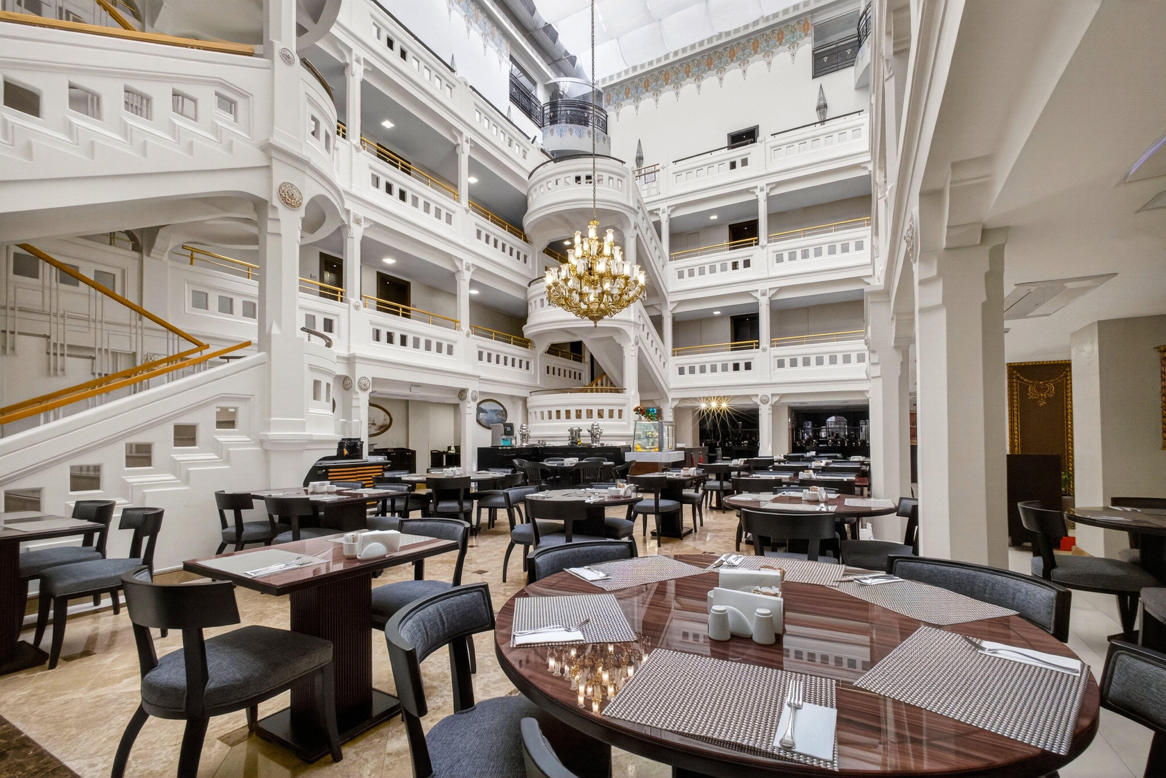 A multi-level hotel lobby with a grand chandelier, multiple dining areas, and a staircase.