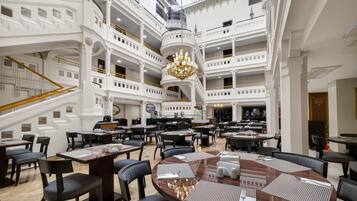 A multi-level hotel lobby with a grand chandelier, multiple dining areas, and a staircase.