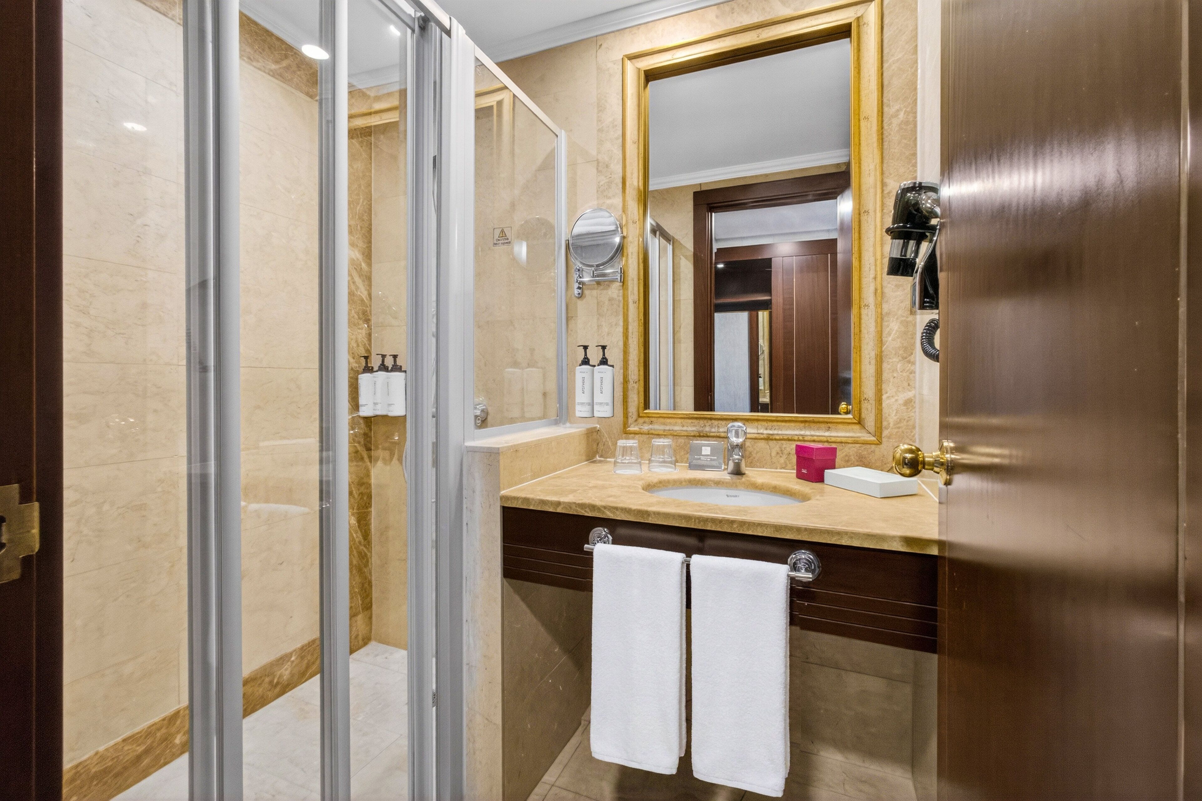 Un baño con cabina de ducha de vidrio, lavamanos con espejo y dos toallas colgadas en un perchero.
