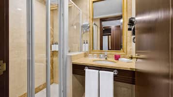 Un baño con cabina de ducha de vidrio, lavamanos con espejo y dos toallas colgadas en un perchero.