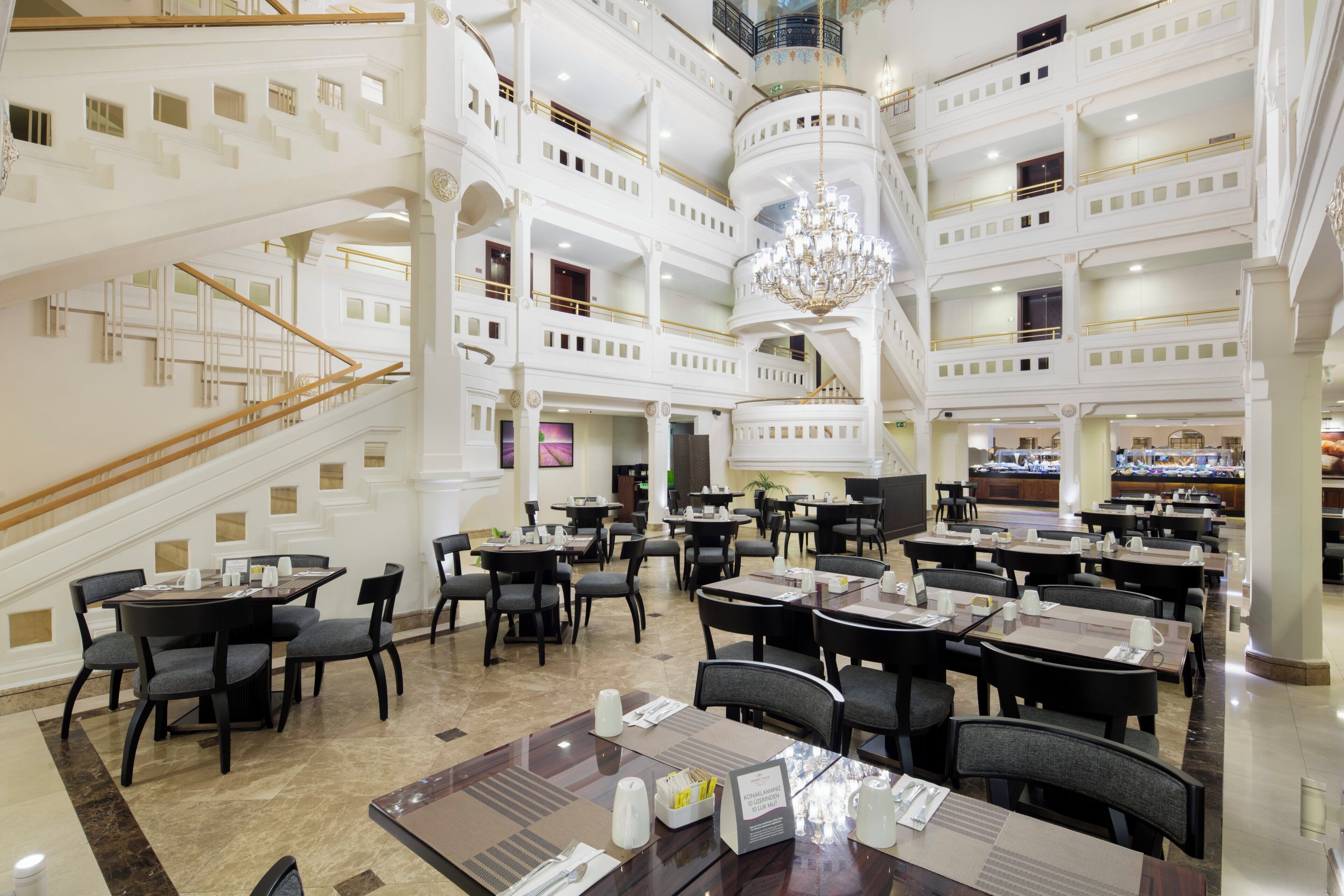 A multi-level hotel lobby with a grand staircase, multiple dining areas, and a chandelier.