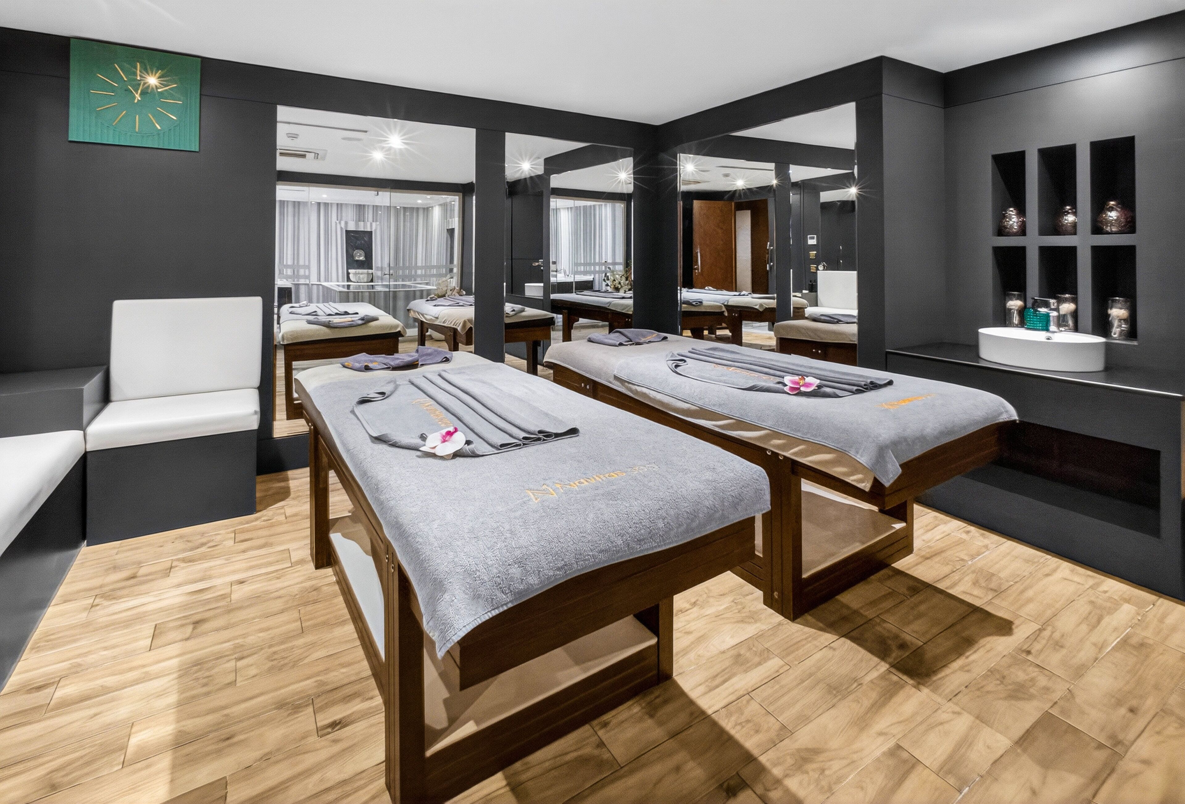 A spa room with two massage tables, a white chair, and a mirror wall.