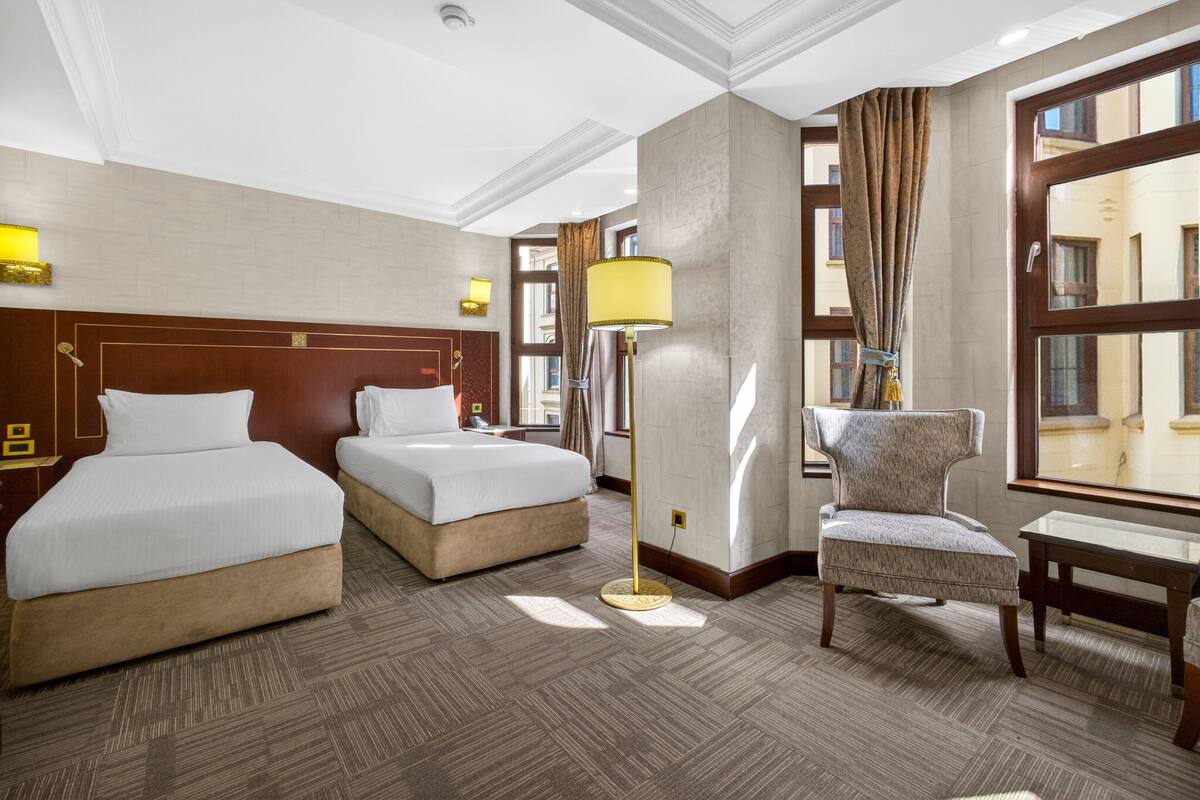 Een hotelkamer met twee bedden, een stoel, een lamp en een groot raam.