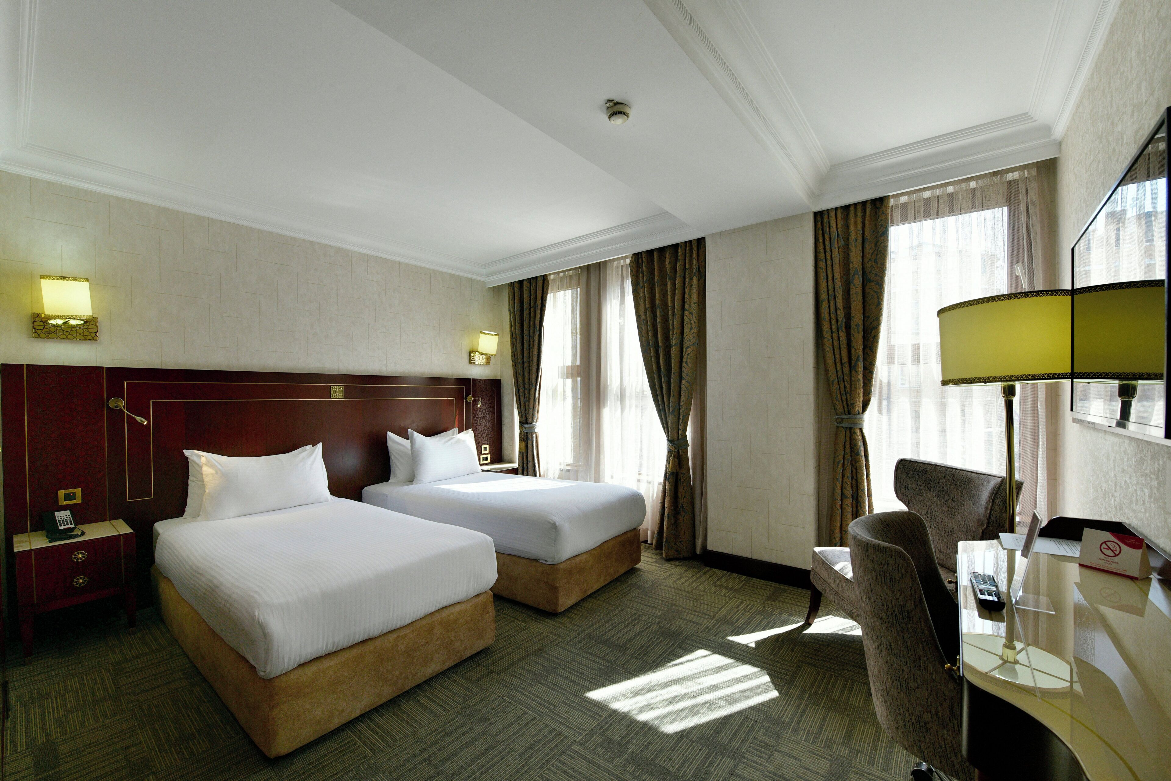 A hotel room with two beds, a desk with a lamp, a chair, a nightstand, and a telephone.