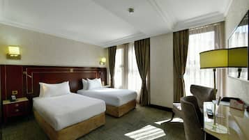 A hotel room with two beds, a desk with a lamp, a chair, a nightstand, and a telephone.