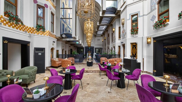 Een hotel lobby met een centrale zithoek, meerdere deuren en een kroonluchter.