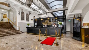 Een hotel lobby met een receptiebalie, een trap en een roodgekleurd tapijt.