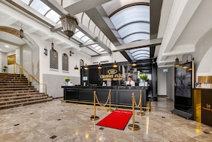 Un hall d’hôtel avec un comptoir d’accueil, un escalier et un tapis rouge.