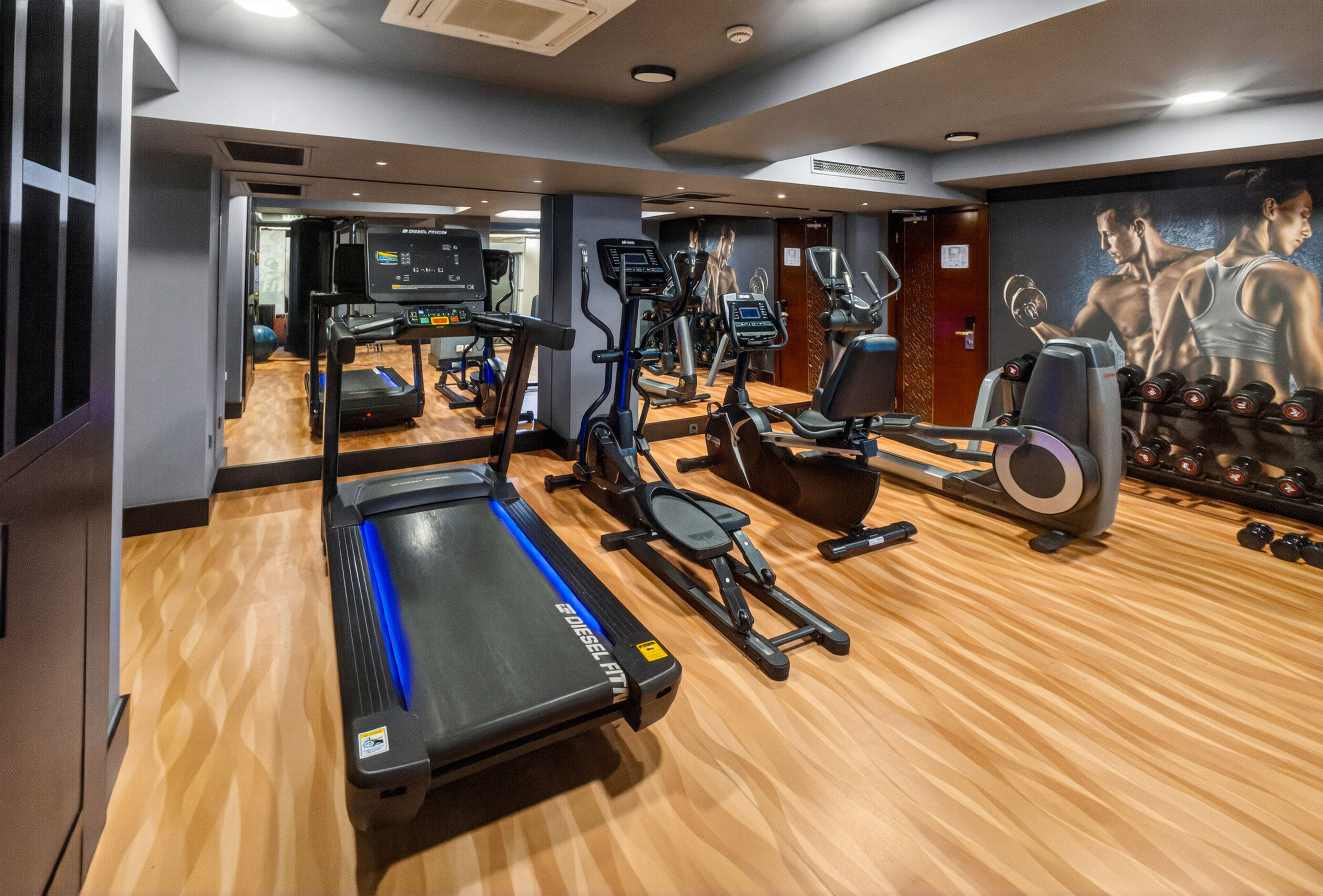 A gym with cardio machines, weight equipment, and a mirrored wall.