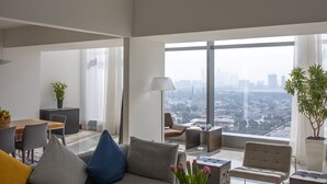 Un salón comedor amplio con techo alto, un ventanal con vistas a la ciudad, un sofá con cojines, una mesa de centro y una zona de comedor con sillas y mesa.