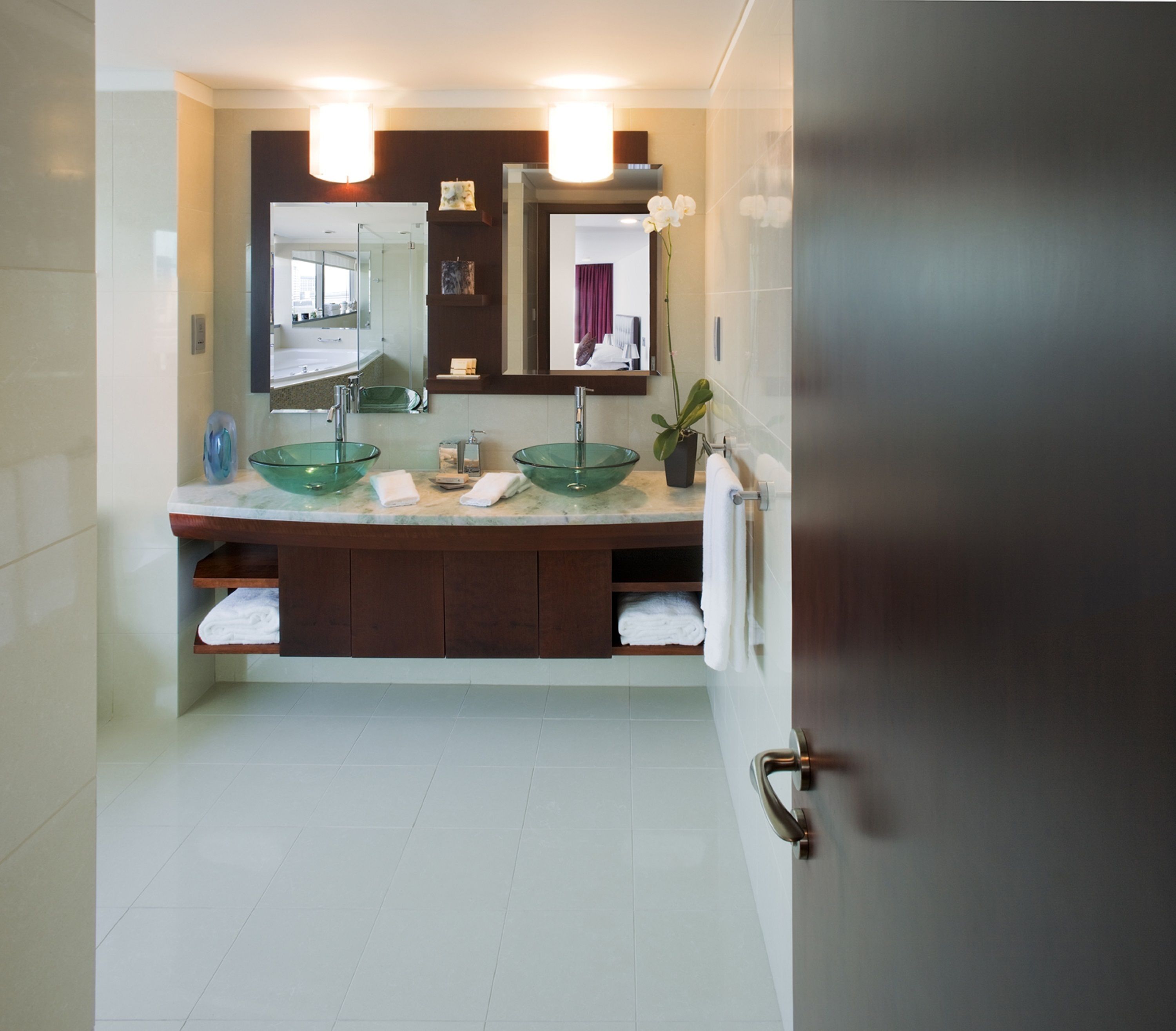 A modern bathroom with two glass sinks, a large mirror, and a potted plant.