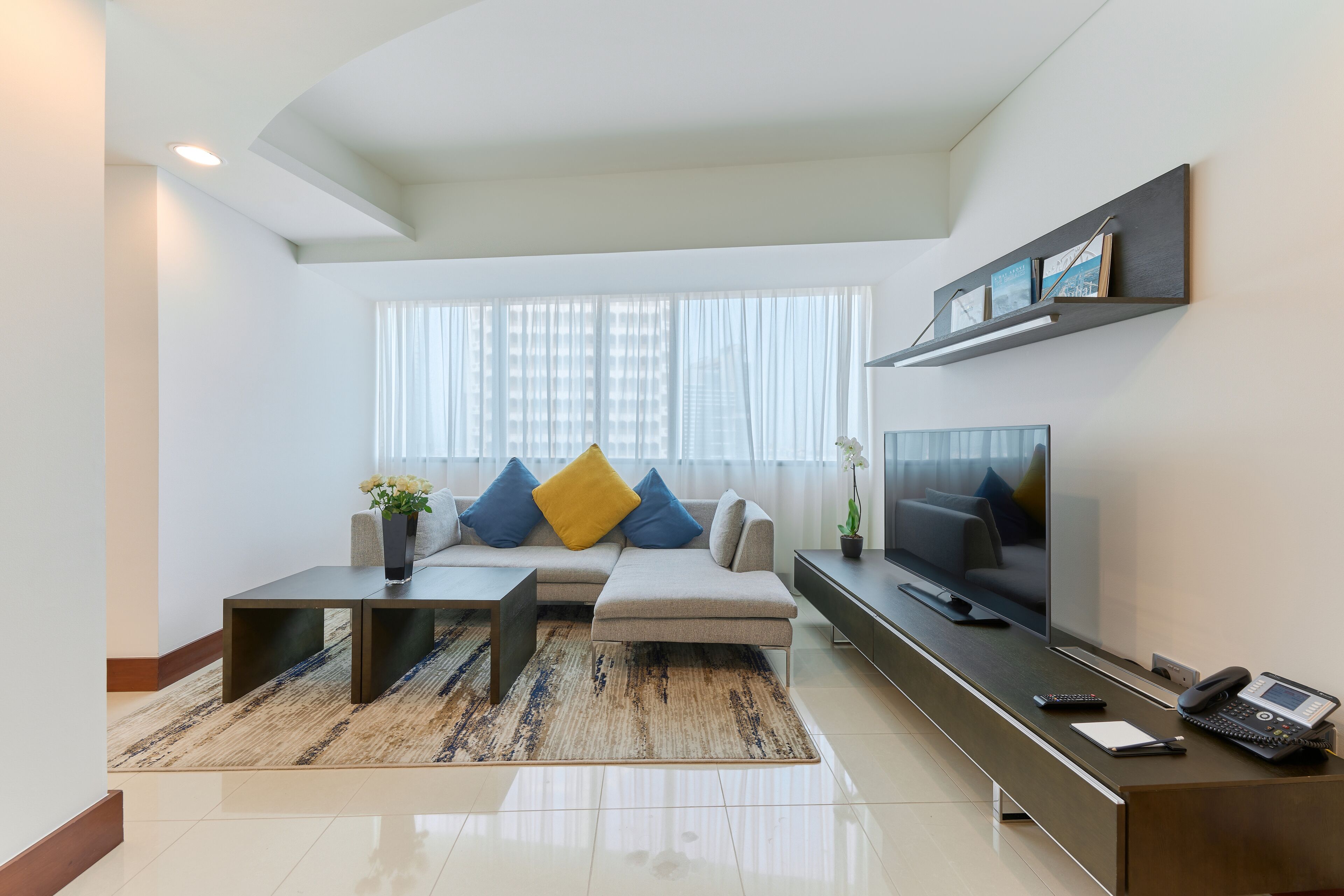 A modern living room with a sectional sofa, a coffee table, a flat-screen TV, and a desk with a telephone.