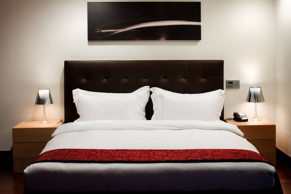 A hotel room with a large bed, two bedside tables, a headboard, a wall-mounted artwork, and a telephone on one of the tables.