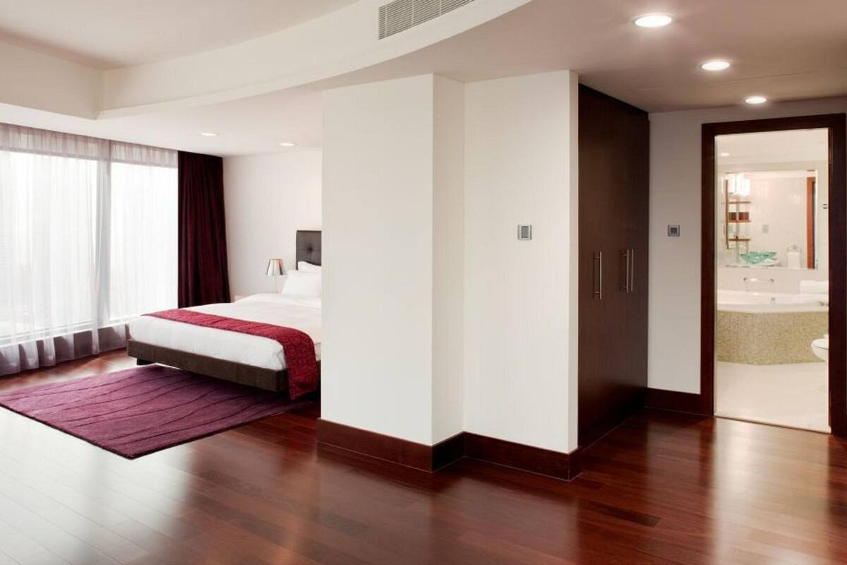 A modern hotel room with a large bed, a walk-in closet, and a bathroom visible through an open door.