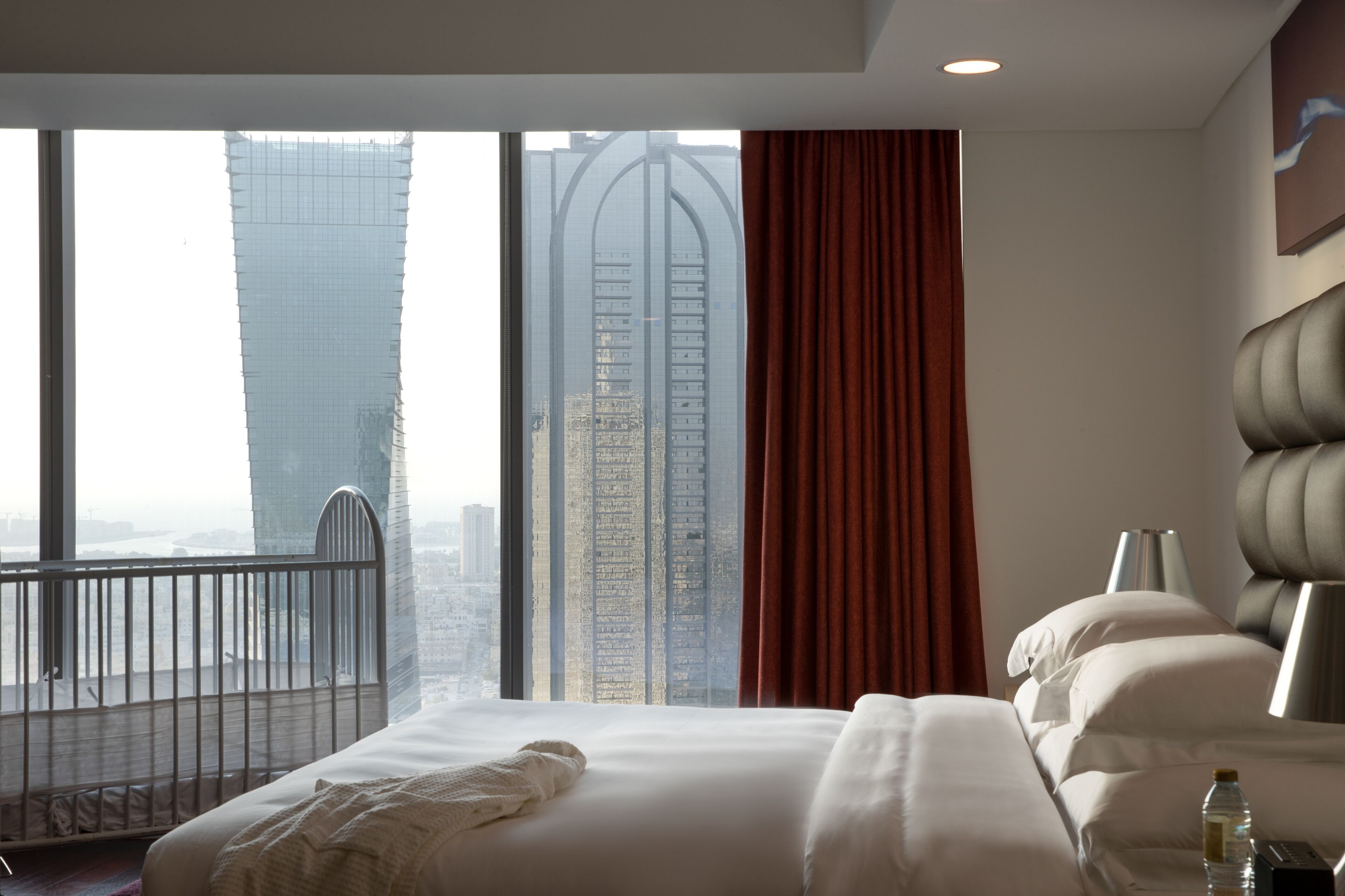 A hotel room with a large bed, a view of tall buildings, and a balcony.