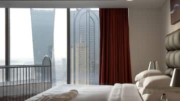 A hotel room with a large bed, a view of tall buildings, and a balcony.