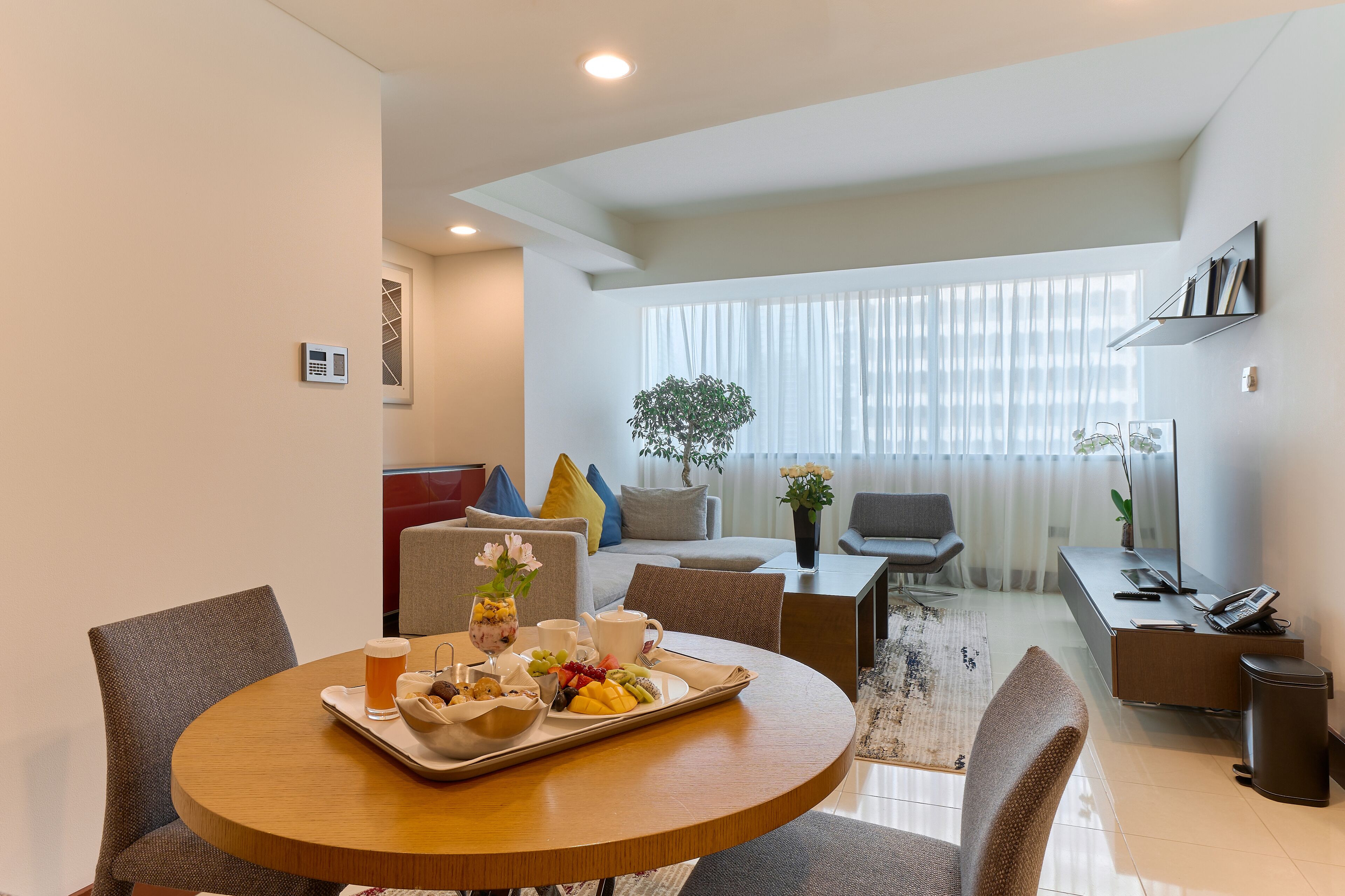 Ein modernes Hotelzimmer mit Essbereich, einer Couch, einem Schreibtisch und einem großen Fenster mit Vorhängen.