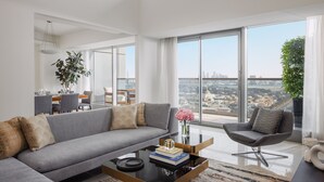 Una sala de estar moderna con un sofá gris, una mesa de centro y vistas de la ciudad a través de amplias ventanas.