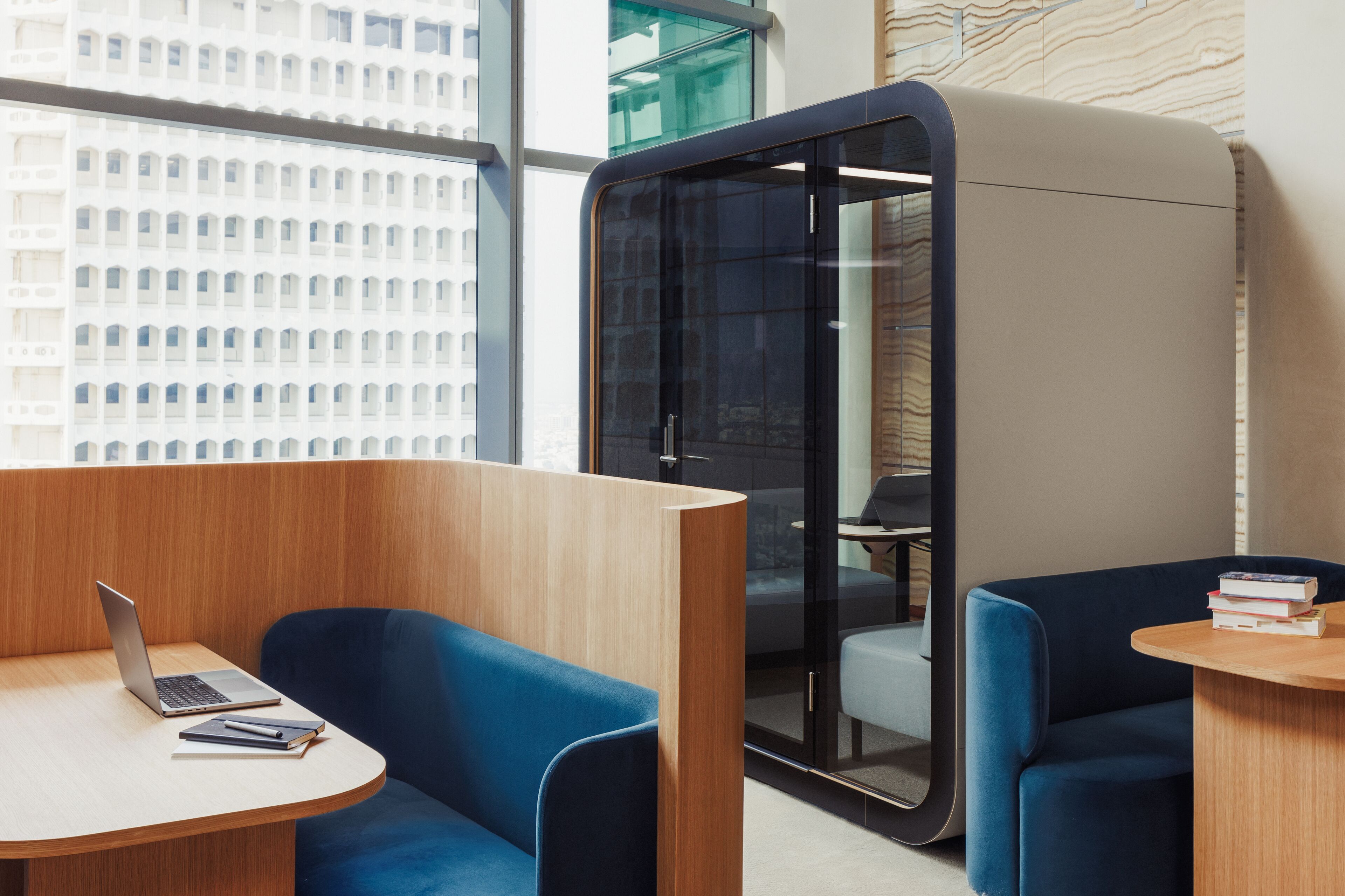 Een moderne kantoorruimte met een laptop op een houten tafel, blauwe stoelen en een glazen scheidingswand.