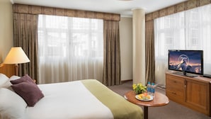 Une chambre d’hôtel avec un lit, une télévision, un bureau avec une assiette de fruits et des rideaux.