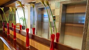 Une rangée de vases rouges ornés de fleurs blanches est disposée sur un comptoir en bois, dans un espace d’accueil.