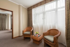 Habitación de hotel con dos sillones de mimbre, una mesita con una bandeja y un ventanal con cortinas de encaje.