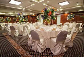 Uma sala de banquetes com mesas redondas, toalhas brancas e cadeiras com capas cinzas.