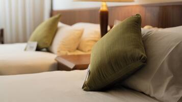 A hotel room with two beds, each with a pillow and a bedside table.