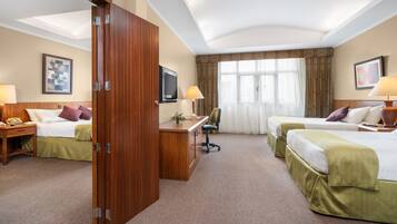 Habitación de hotel con dos camas, un escritorio, una silla, un televisor y una ventana con cortinas.