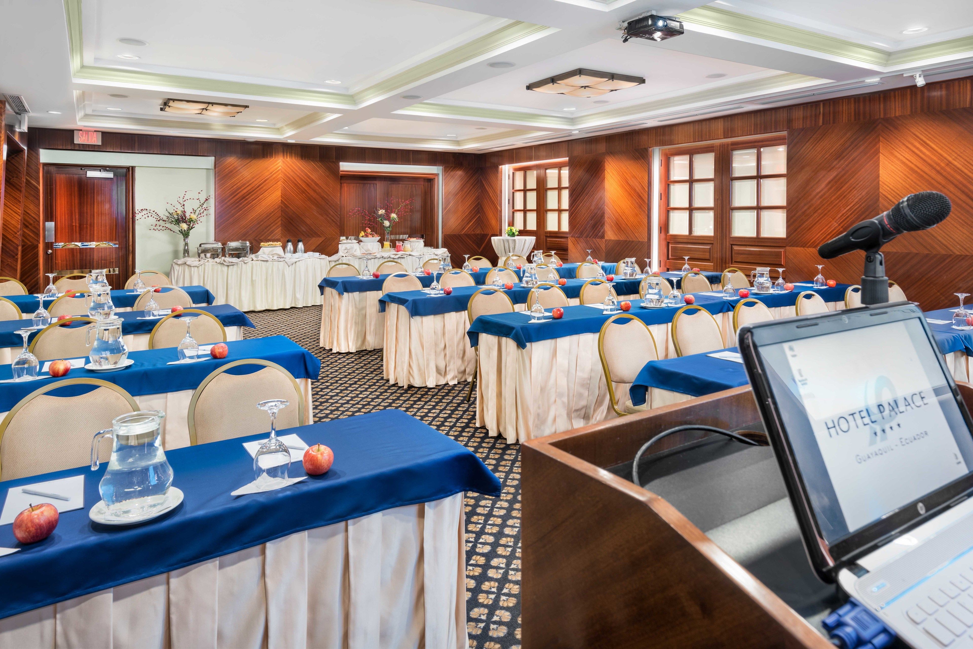 A conference room with tables set for a meeting, a podium with a laptop, and a wooden wall panel design.