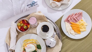 A breakfast tray with eggs, ham, cheese, croissants, and fruit on a hotel bed.