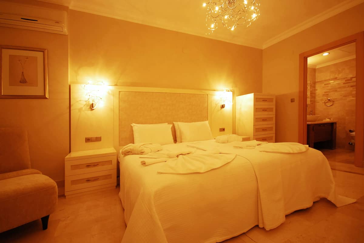 A hotel room with a large bed, bedside tables, a chair, and a chandelier.