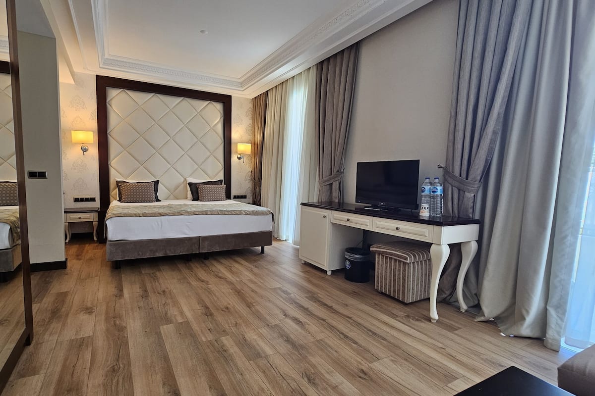 A hotel room with a bed, a desk with a TV, a chair, and a small trash bin.