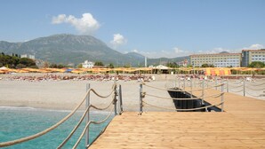 Een houten steiger die naar een strand loopt, met parasols en mensen.