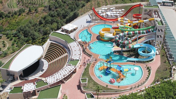 Een waterpark met diverse glijbanen en zwembaden, een groot openluchttheater en een bus voor transport.