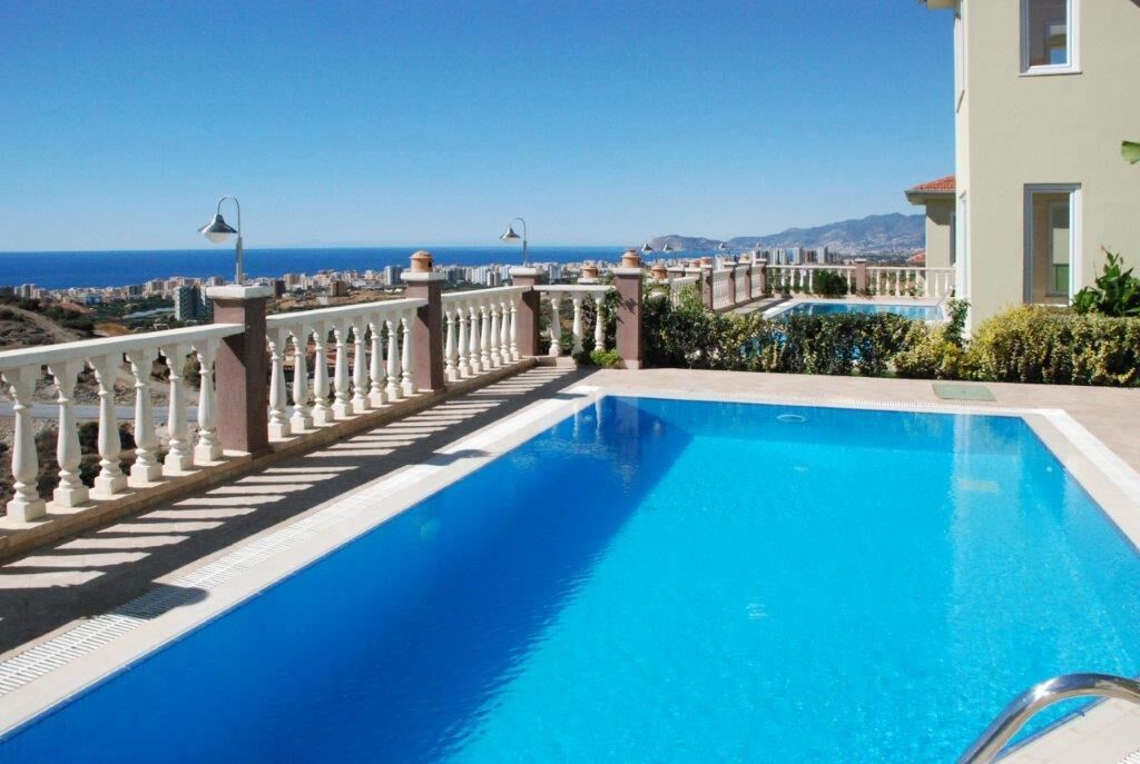 A swimming pool with a white balustrade and a view of the sea and cityscape.