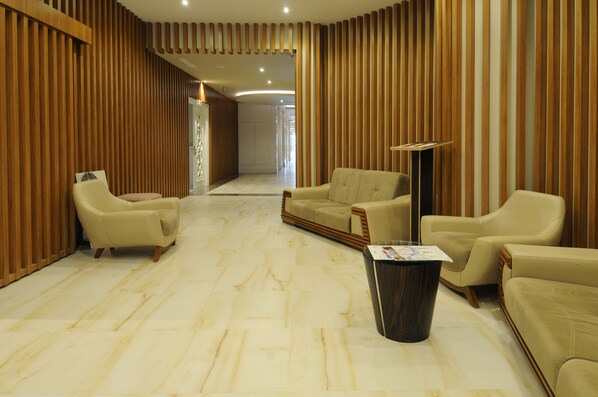 A hotel lobby with a marble floor, beige sofas, a coffee table, and wooden paneling on the walls.